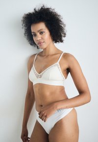 Lys beige bh med trekantkopper, mesh-detaljer og prikkete mønster, sammen med matchende hvite truser med logo-band.