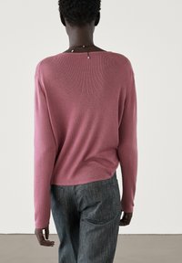 Haut à manches longues rose avec une texture cannelée, coupe ample et encolure large, associé à un pantalon texturé gris foncé.