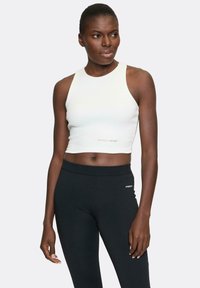 White crop top with a high neckline, paired with black leggings. The top features subtle branding; leggings have a fitted design and logo accent.