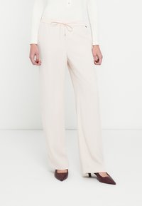 Pantaloni largi bej deschis cu talie ajustabilă prin șnur, confecționați dintr-un material neted. Asortați cu pantofi cu toc cui burgund în vârf ascuțit pentru contrast.