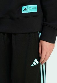 Schwarzer Pullover mit türkisfarbenen Akzenten und Markenlogo. Sportliche Hose mit türkisfarbenen Seitenstreifen und Logo. Glatte Stofftextur mit gerippten Bündchen.