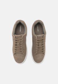 Brune ruskinnssneakers med en teksturert finish, med beige snøringer og hvite gummisåler. Minimalistisk design med en logo innvendig.