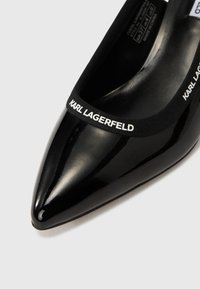 Čierny lodičky z lakovanej kože so špicatou špičkou, vybavené čiernou elastickou páskou s nápisom „KARL LAGERFELD“ pre detail a kontrast.