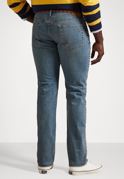 Blå denimjeans med rett benpassform, sydd baklommer og et flettet belte. Parret med hvite lerretsko.