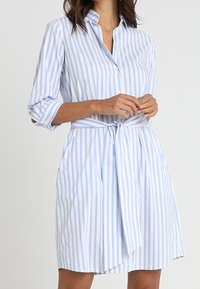 Abito camicia a righe blu e bianche con colletto, chiusura a bottoni, cintura in vita e maniche a tre quarti; realizzato in tessuto leggero.