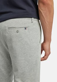Light gray cotton trousers with a back pocket featuring a button, accented by a tri-color stripe. Smooth texture and tailored fit.