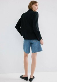 Blazer negru cu dungi fine și design structurat, asortat cu pantaloni scurți din denim albastru mediu. Pantofi negri fără toc completează ținuta.