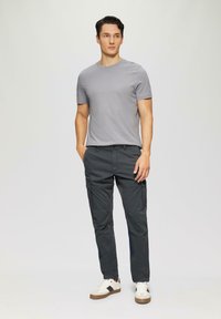Grijze crewneck t-shirt gecombineerd met donkere cargo shorts. De cargo shorts hebben zijzakken. Het model draagt witte sneakers met bruine accenten.