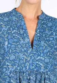 Blaues Blumenmuster-Kleid mit V-Ausschnitt, gerafftem Rock und weichem Baumwollstoff mit hellgrünen Akzenten.