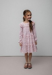 Różowa sukienka w kwiaty z falbanami na kołnierzu i rękawach, warstwowa konstrukcja, miękki materiał, zestawiona z brązowymi butami typu Mary Jane i jasnymi skarpetkami.