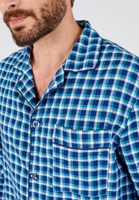 Blauwe en groene geruite pyjamajack met een zak, knoopsluiting en een kraag. Gemaakt van zachte stof met een geruit patroon.