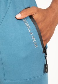 Teal sportbroek met een ritszak. Voorzien van een zwarte rits en een grijze bedrukte 'GORILLA WEAR' label op het zakgedeelte.