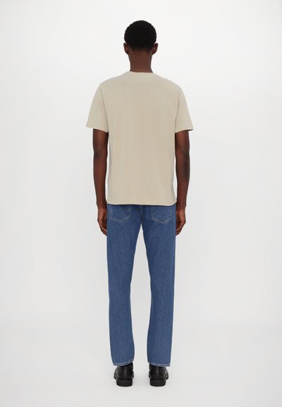 Camiseta de algodón beige con cuello redondo, combinada con jeans de mezclilla azul. Diseño simple, corte recto y colores sólidos. Zapatos negros completan el look.