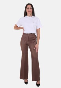 T-shirt bianca a maniche corte con un piccolo logo, abbinata a pantaloni marroni a zampa d'elefante a vita alta e décolleté nere con punta affilata.