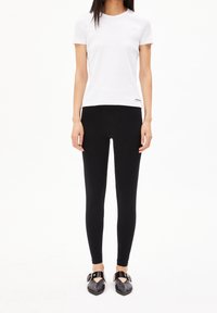 Vit kortärmad bomullströja matchad med svarta leggings. Svarta platta skor med spänne fulländar outfiten. Enkel och figurnära design.