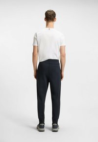 Valkoinen lyhythihainen paita yhdistettynä tummansinisiin joustaviin vyötärönauhallisiin joggereihin. Joggereissa on takatasku ja kapeat lahkeet, sekä sileä pinta.