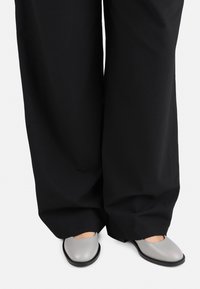 Graue flache Schuhe mit runder Spitze, präsentiert mit weiten schwarzen Hosen. Glatte Textur mit matter Oberfläche und minimalistischem Design.