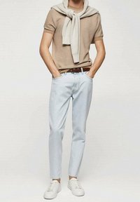 Camisa beige de manga corta con relieve, jeans azul claro ajustados, zapatillas blancas y un suéter gris claro colgado del cuello.