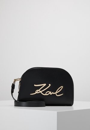 Black leather crossbody bag with a curved shape, featuring a prominent gold embossed "Karl" logo and a detachable strap.