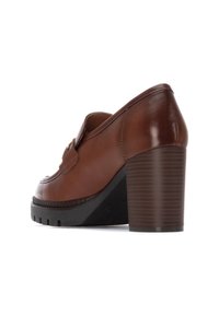 Zapato de tacón de cuero marrón con punta redondeada, suela de goma y tacón apilado texturizado. Presenta una correa decorativa a lo largo del empeine.