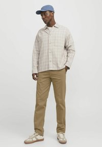 Light plaid shirt with a buttoned front, tan chinos, and beige sneakers. A blue cap complements the outfit, featuring simple, structured designs.