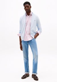 Lichtblauwe cardigan over een roze en witte gestreepte shirt, lichte denim jeans, en donkerbruine instappers. Soepele texturen en casual design.