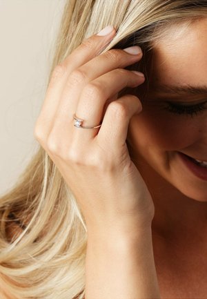 Silberring mit einem klaren Edelstein in einem eleganten, minimalistischen Design; Hand, die sanft das Haar berührt, mit heller Hautfarbe.