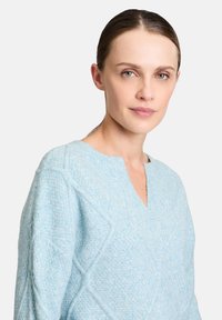 Hellblau gestrickter Pullover mit V-Ausschnitt, der ein strukturiertes Muster und Rautenmuster aufweist. Weiches Material und lockere Passform.
