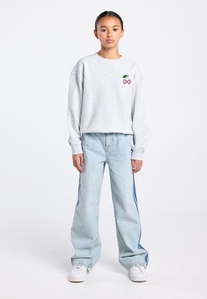 Grijze trui met kersenborduursel op de borst, gecombineerd met lichtblauwe wijde jeans met donkere strepen aan de zijkant en witte sneakers.