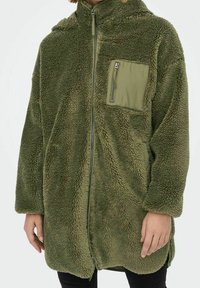 Zelená plyšová mikina na zip, s kapucí a čtvercovou kapsou na hrudi. Texturovaná látka a volný střih.