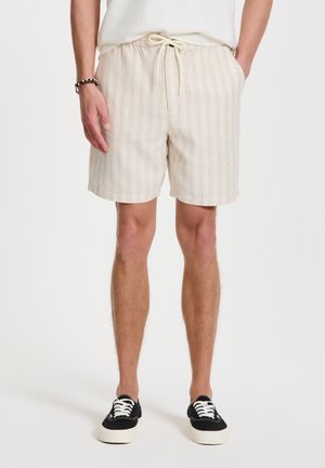 Lichtbeige gestreepte heren shorts met een koord in de taille, gemaakt van een gestructureerde stof. Gepaard met zwarte sneakers met witte veters.