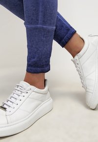 Vita sneakers med tjocka sulor, texturerat läder och fem snörhål. Bärs med blå, åtsittande ankel-långa leggings med en gradienteffekt.