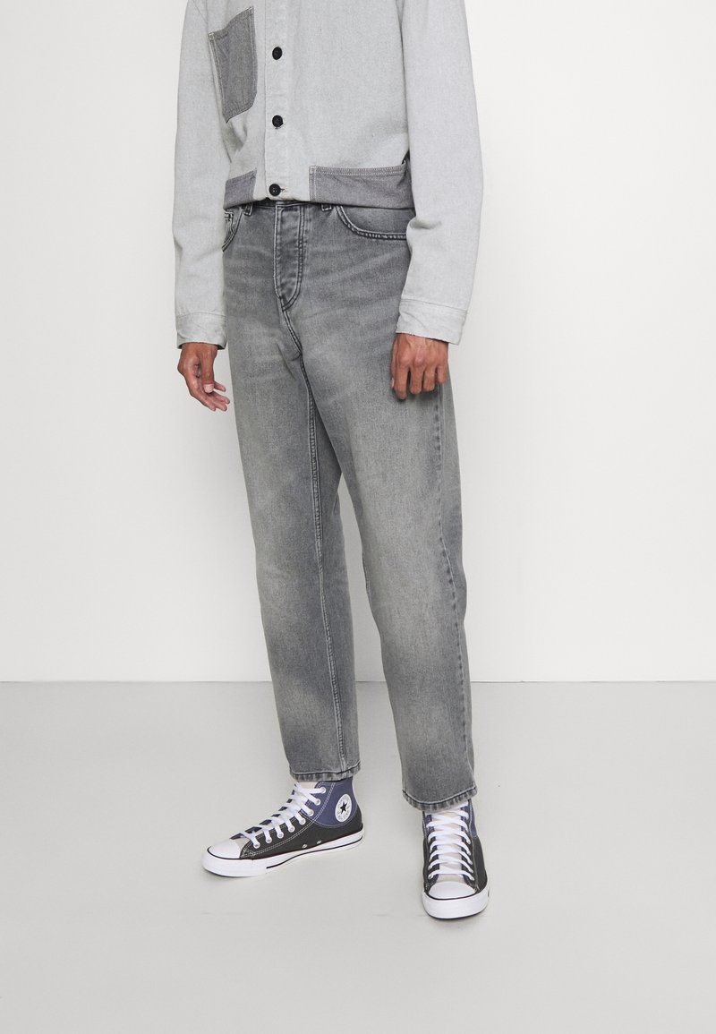 Jasnoszare jeansy z denimu o prostym kroju nogawek, z wyblakłymi miejscami. Do tego szaro-czarne trampki za kostkę z widocznymi białymi sznurowadłami.