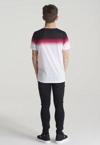Camiseta de manga corta con un degradado de negro a rojo y blanco, hecha de una tela suave. Se combina con jeans negros ajustados y zapatillas negras.