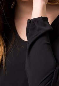 Blusa nera con maniche lunghe e dettagli arricciati sui polsini, texture morbida e scollatura rotonda.