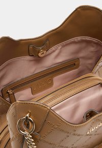 Sac à main en cuir brun avec des accessoires en métal doré, présentant une texture lisse et des détails de logo estampés. L'intérieur comprend une doublure rose et des poches zippées.