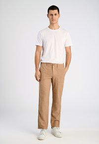 Lättbeiga linnebyxor med rak passform, utrustade med knäppning och två framfickor. Matcher med en vanlig vit t-shirt och vita sneakers.