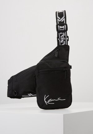 Black crossbody bag with two zippered compartments and adjustable strap featuring white graphic text and signature detail on front pocket.