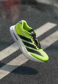 Groene en zwarte sportschoen met een mesh-bovenkant, drie zwarte strepen, lichtgewicht ontwerp, afgeronde zool en minimalistische branding.