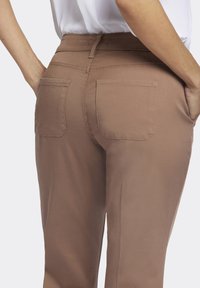 Pantalon marron avec poches arrière, texture lisse et design ajusté, présenté de profil avec une taille plate.