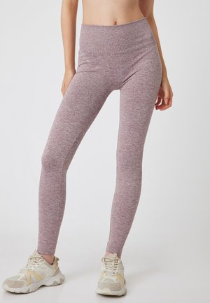 Leggings en una tela rosa jaspeada con una cintura alta, que presentan un diseño ajustado y material elástico. Combinados con zapatillas deportivas beige y blancas.