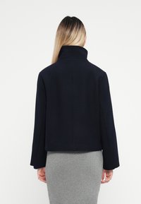 Marineblå cropped jakke med høj krave, lavet af et tekstureret stof. Har brede ærmer og et sømløst rygdesign.