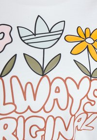 Vitt tyg med färgglada blommönster: en rosa blomma, en blårandig blomma och en gul blomma, med gröna blad och fet orange text.