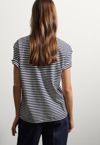 Camiseta de rayas en azul marino y blanco con mangas cortas arremangadas, corte relajado, tela suave y dobladillo curvado, combinada con pantalones oscuros.