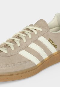 Baskets Adidas Spezial en daim beige avec bandes blanches, lacets crème et semelle en gomme.