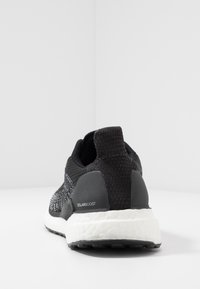 Chaussure de sport noire avec une tige en tricot, des détails en maille texturée, un capuchon de talon en caoutchouc et une semelle à amorti Boost blanche. Modèle : Solarboost.
