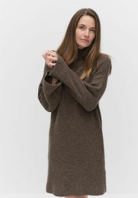 Brun tröjdress med hög hals, långa ärmar och ett strukturerat stickat mönster. Tyget verkar mjukt och något oversized.