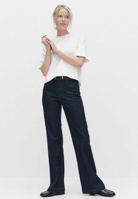 Valkoinen lyhythihainen cropped-t-paita yhdistettynä tummansinihin leveälahkeisiin farkkuihin ja mustiin kenkiin. Yksinkertainen muotoilu, sileä rakenne ja minimaalinen yksityiskohtaisuus.