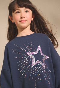 Felpa blu navy con un motivo a stella realizzato con paillettes lucenti e motivi irradianti. Tessuto morbido con vestibilità comoda e scollo rotondo.