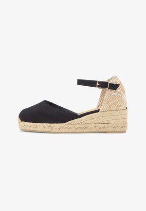Mule compensée en toile noire avec semelle en jute tressé, contrefort beige tressé et bride de cheville noire avec boucle dorée.